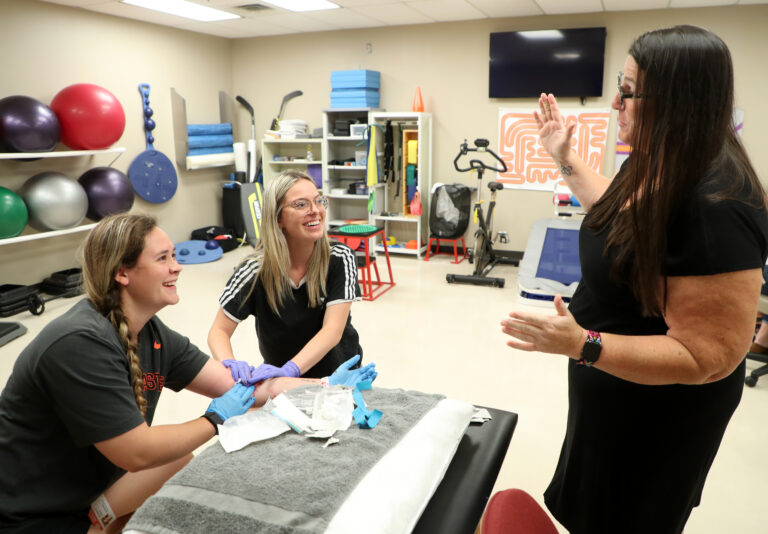 Instructors helps students as they practice using an IV line in the athletic training lab at the OSU Center